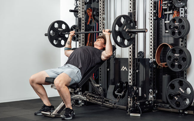 An athlete incline bench pressing off the front of the Wall-Mounted Ares™ 2.0 while laying on a REP BlackWing™ bench