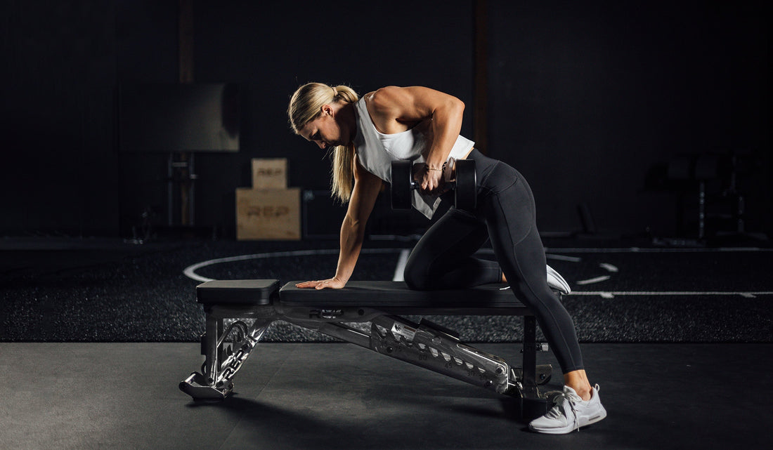 A woman tackles a row while stabilizing herself on an adjustable bench.