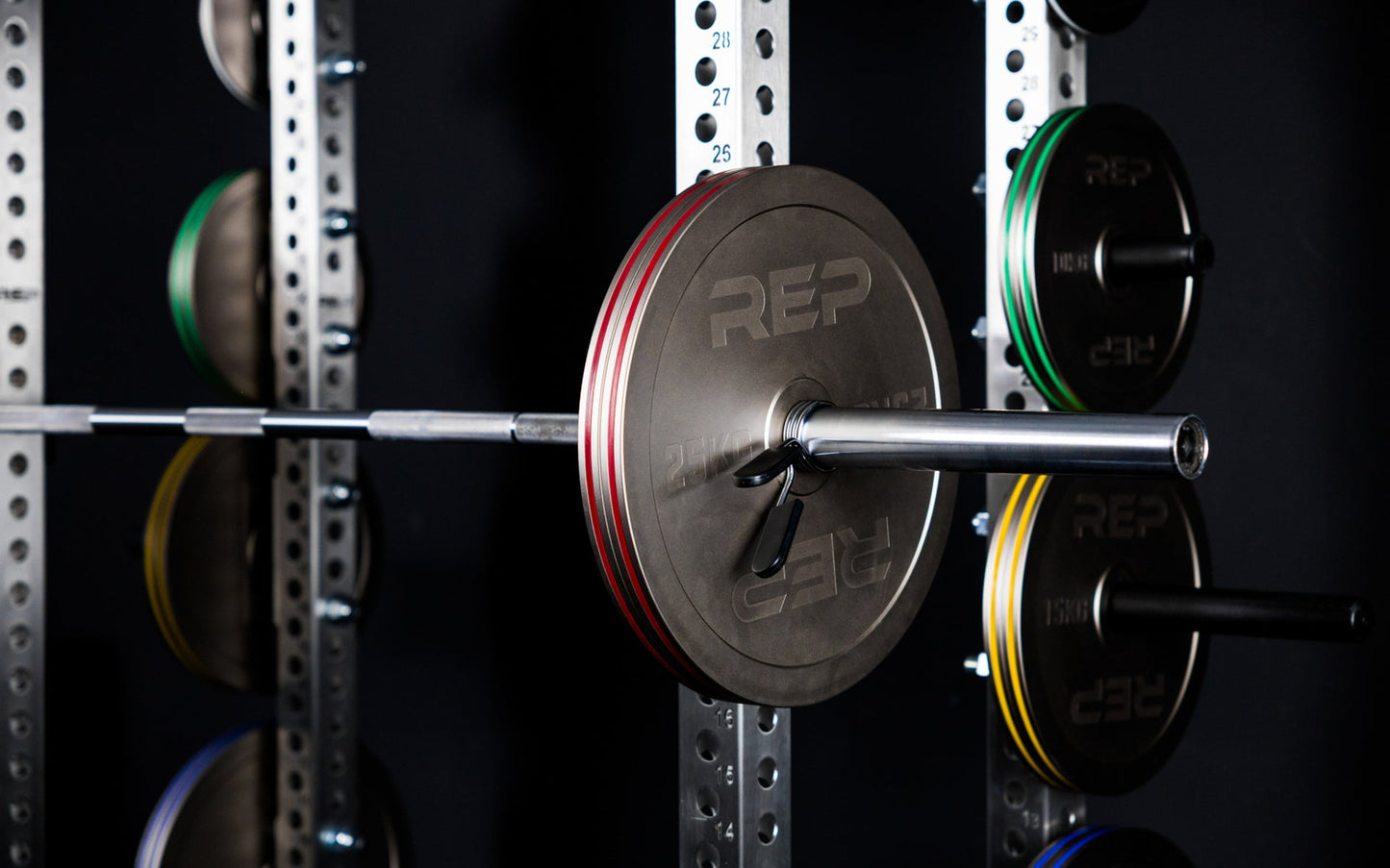 Rep Fitness Calibrated Steel Plates (KG) loaded on a barbell and on weight horns on a PR-5000 rack, highlighting their colored banding